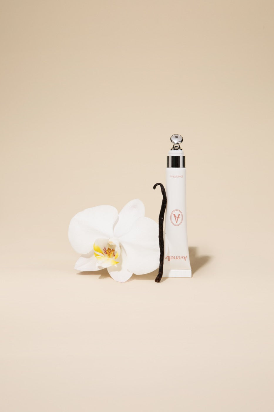 Vanilla lip balm beside a white orchid and a vanilla bean