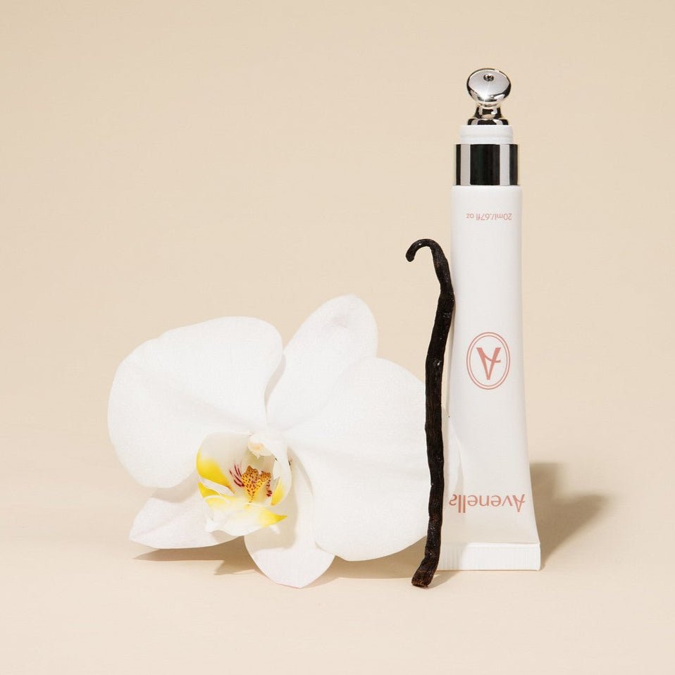 Avenella Vanilla lip balm beside a white orchid and a vanilla bean