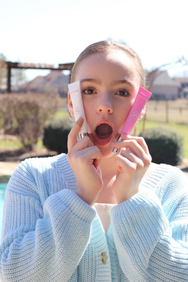 Aliya holding her Avenella lip balms outdoors
